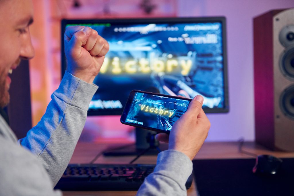Victory text on a screen, a happy man celebrating he has won. Streamer playing FPS shooter game at home. The joy of playing games and earning some crypto.
