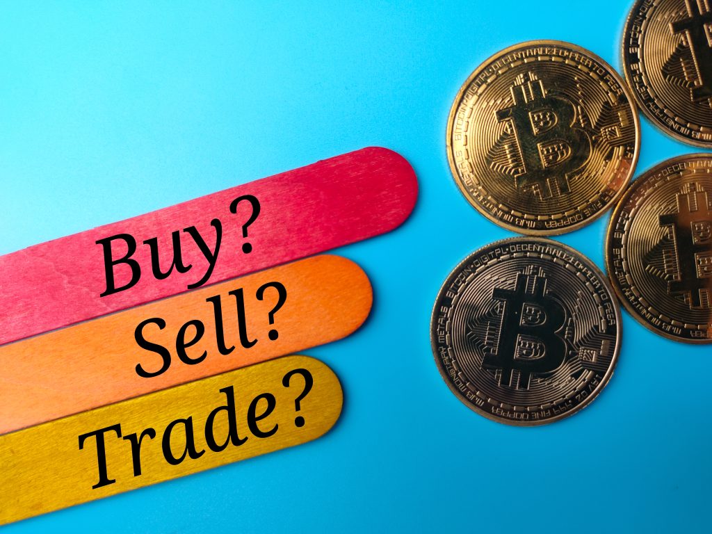 Bitcoins and colored ice cream sticks with text BUY SELL TRADE on blue background.