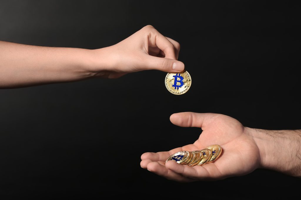 Hand of woman putting golden bitcoin on man's palm against dark background