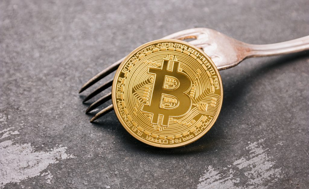 Bitcoin Cash (BCH) dorado en un tenedor plateado sobre fondo oscuro, imagen conceptual para una bifurcación (fork) de bitcoin. ideal para sitios web y revistas