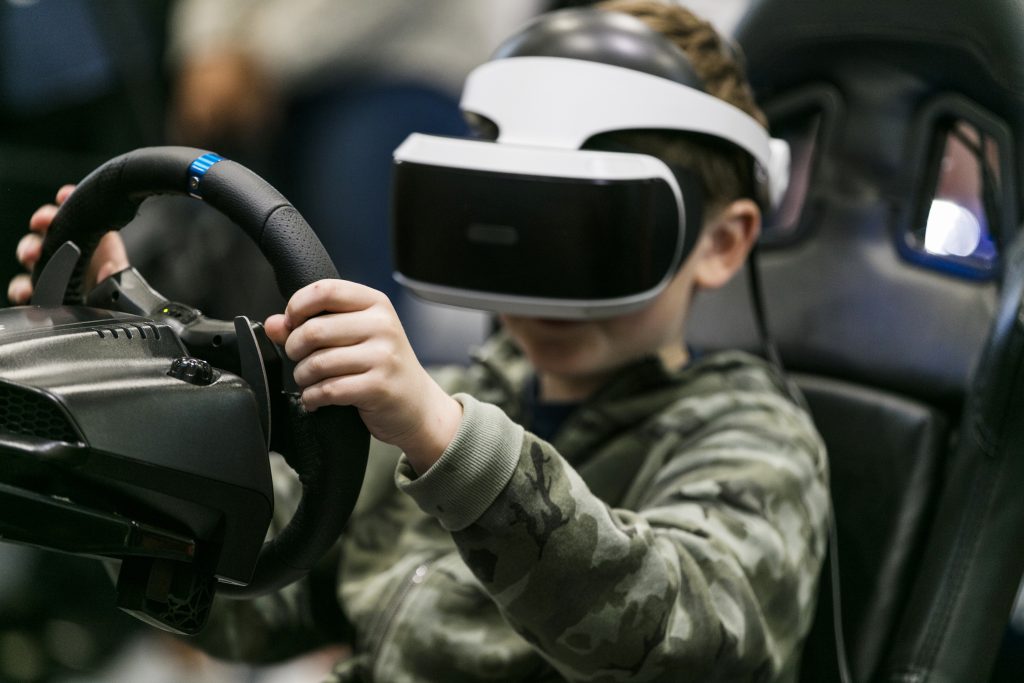A boy wearing a Virtual Reality headset plays a racing game among the different types available
