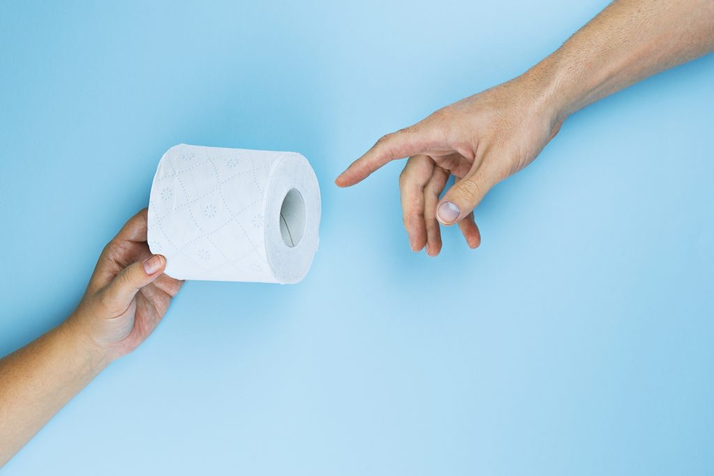 Paper hands in crypto representation. Female hand gives toilet paper roll to male hand on blue background, top view, flat lay. Panic buying due to outbreak coronavirus. Prank creation of Adam metaphor by Michelangelo