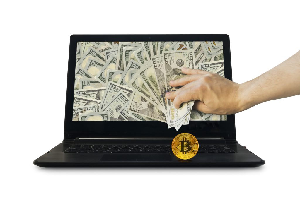 lavado de dinero a través de criptomonedas, laptop llena de dinero con moneda bitcoin