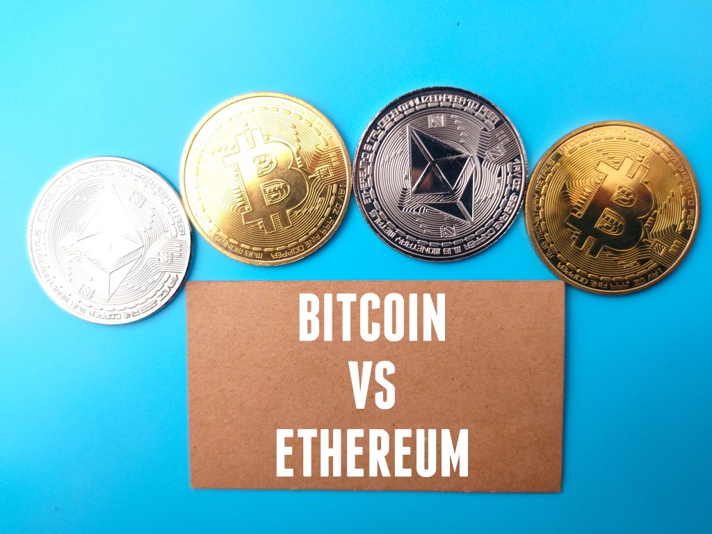 Golden bitcoin, silver ethereum and brown card with text BITCOIN VS ETHEREUM on blue background.