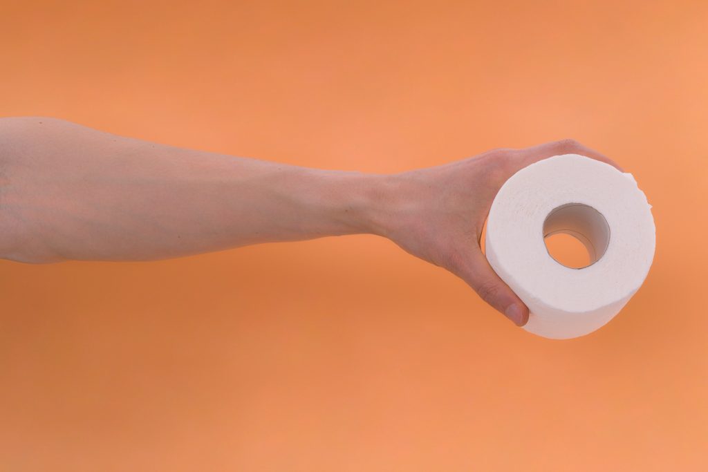 toilet paper representing crypto term. Man hand holding toilet paper on orange background. 