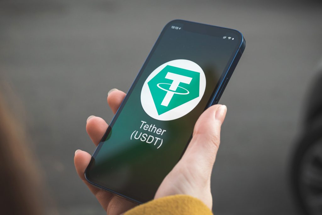 Tether USDT cryptocurrency symbol, logo. Business and financial concept. Hand with smartphone, screen with crypto icon closeup