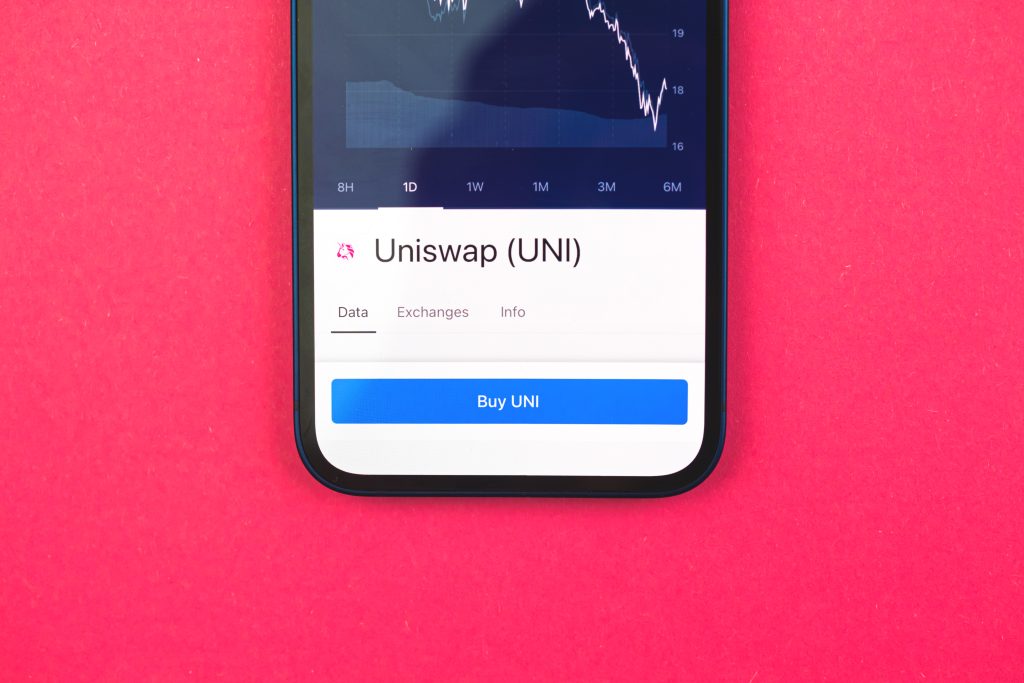Buy Uniswap UNI crypto currency, mobile phone app with button, concept of online trade, investment and coin exchange with smartphone, finance, office desk top view photo