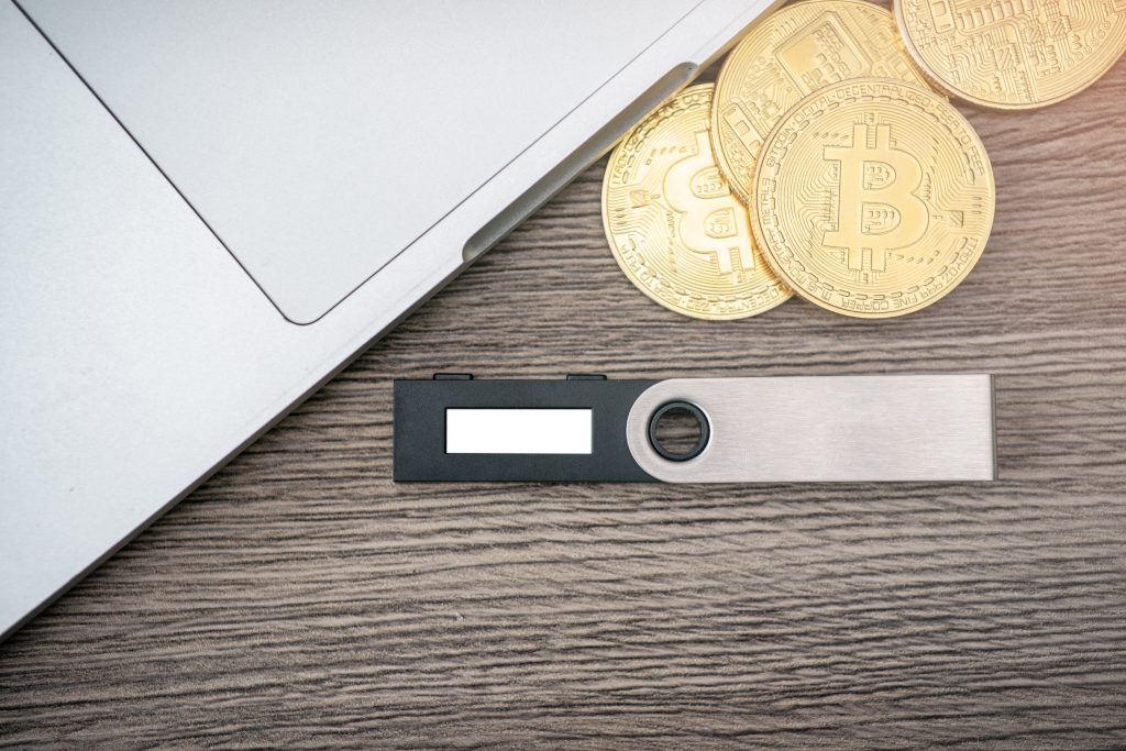 Hardware cryptocurrency wallet with golden Bitcoin (BTC) and computer. Safe storage for crypto.